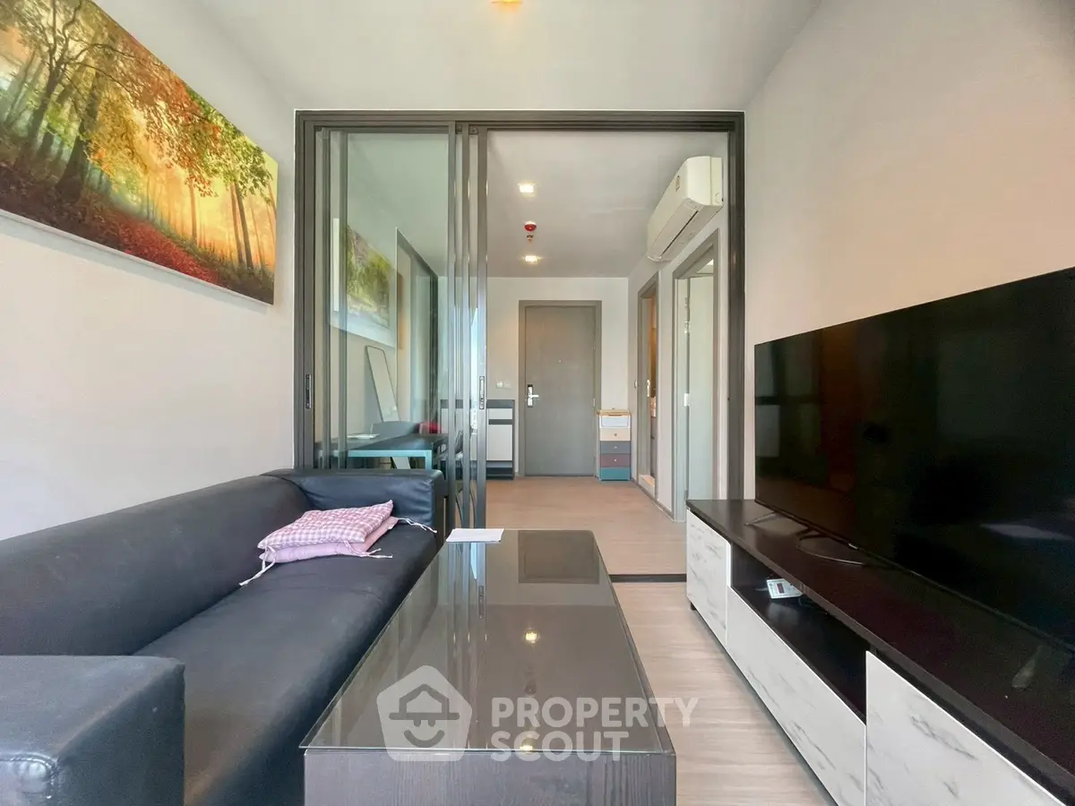 Modern living room with sleek black sofa, large TV, and vibrant wall art in a stylish apartment.
