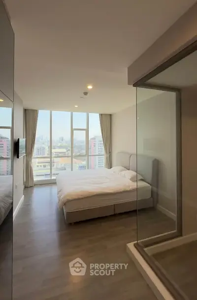 Spacious modern bedroom with large windows offering stunning city views, featuring elegant decor and natural light.