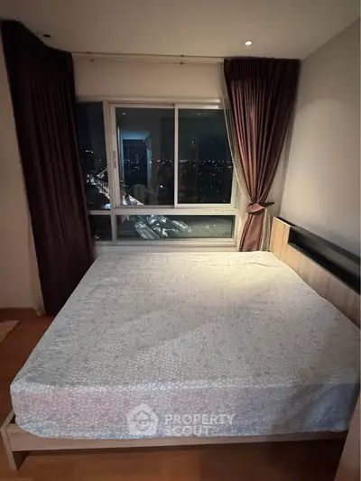 Cozy bedroom with large window offering stunning city night view, perfect for relaxation and comfort.
