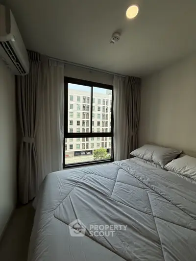 Cozy bedroom with large window offering city view, featuring a comfortable bed and elegant curtains.