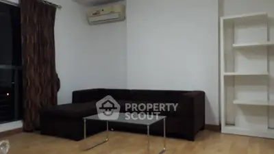 Modern living room with dark sofa and glass coffee table, featuring air conditioning and wooden flooring.