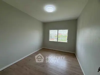 Spacious empty room with wooden flooring and large window, perfect for customization.