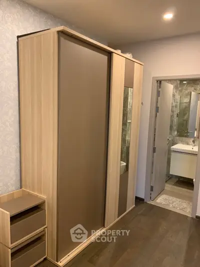 Modern bedroom with sleek wardrobe and en-suite bathroom, featuring elegant wood flooring.