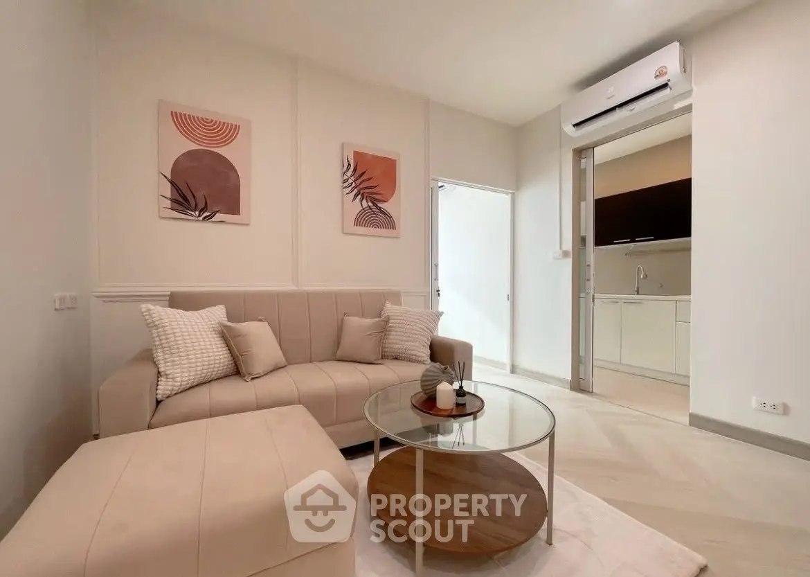 Modern living room with stylish decor and open kitchen layout, featuring a cozy beige sofa and glass coffee table.