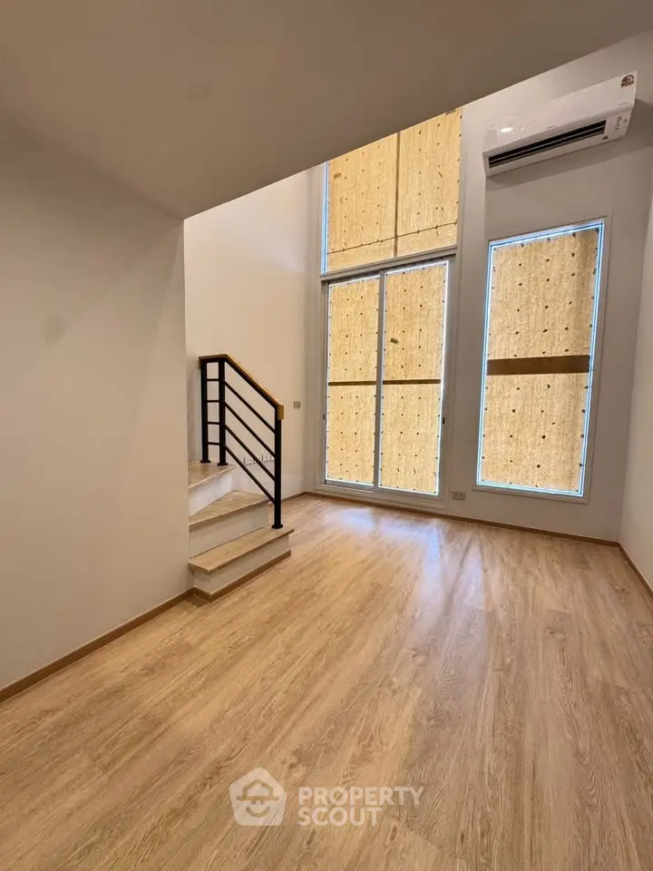 Spacious modern living room with high ceilings and wooden flooring, featuring large windows and a sleek staircase.