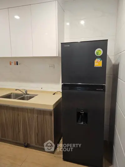 Modern kitchen with sleek black fridge and dual sink in stylish apartment.