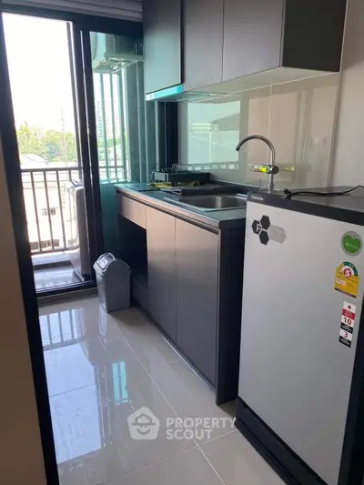 Modern kitchen with sleek cabinets and balcony view, featuring energy-efficient fridge and ample natural light.