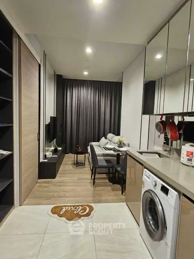 Modern living room with open kitchen and washing machine, featuring sleek design and cozy ambiance.