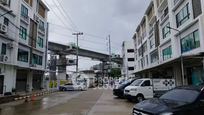 Modern urban building complex with parking area and elevated train tracks in the background.