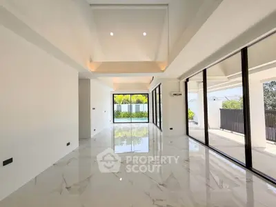 Spacious modern living room with marble flooring and large windows overlooking a pool area.