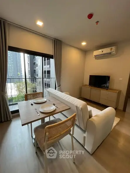 Modern living room with balcony view in a high-rise apartment, featuring sleek furniture and natural light.
