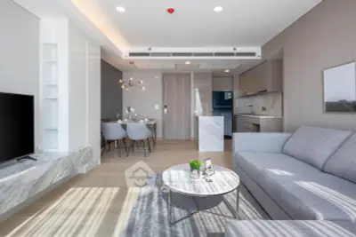 Modern open-plan living room with sleek kitchen and dining area, featuring stylish furniture and natural light.