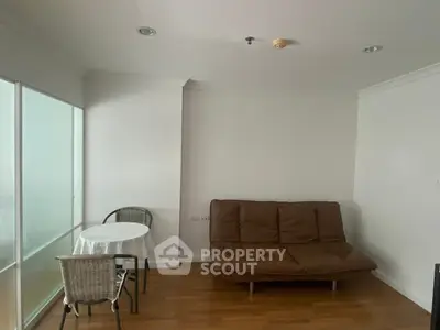 Cozy living room with brown sofa and dining table, featuring wooden flooring and white walls.