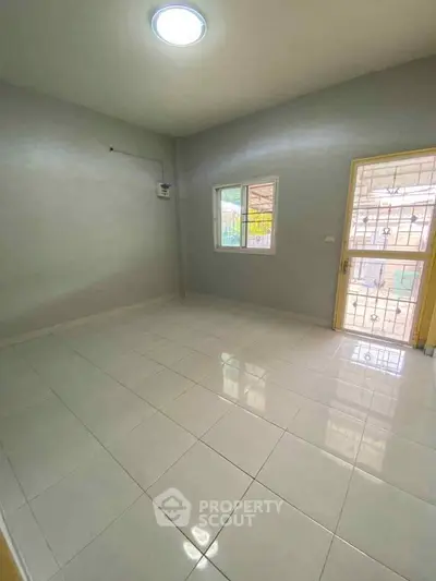 Spacious empty room with tiled flooring and natural light, featuring a window and a door leading outside.