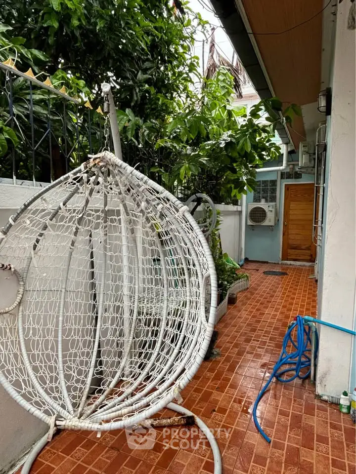 Charming outdoor patio with hanging chair and lush greenery, perfect for relaxation and outdoor enjoyment.