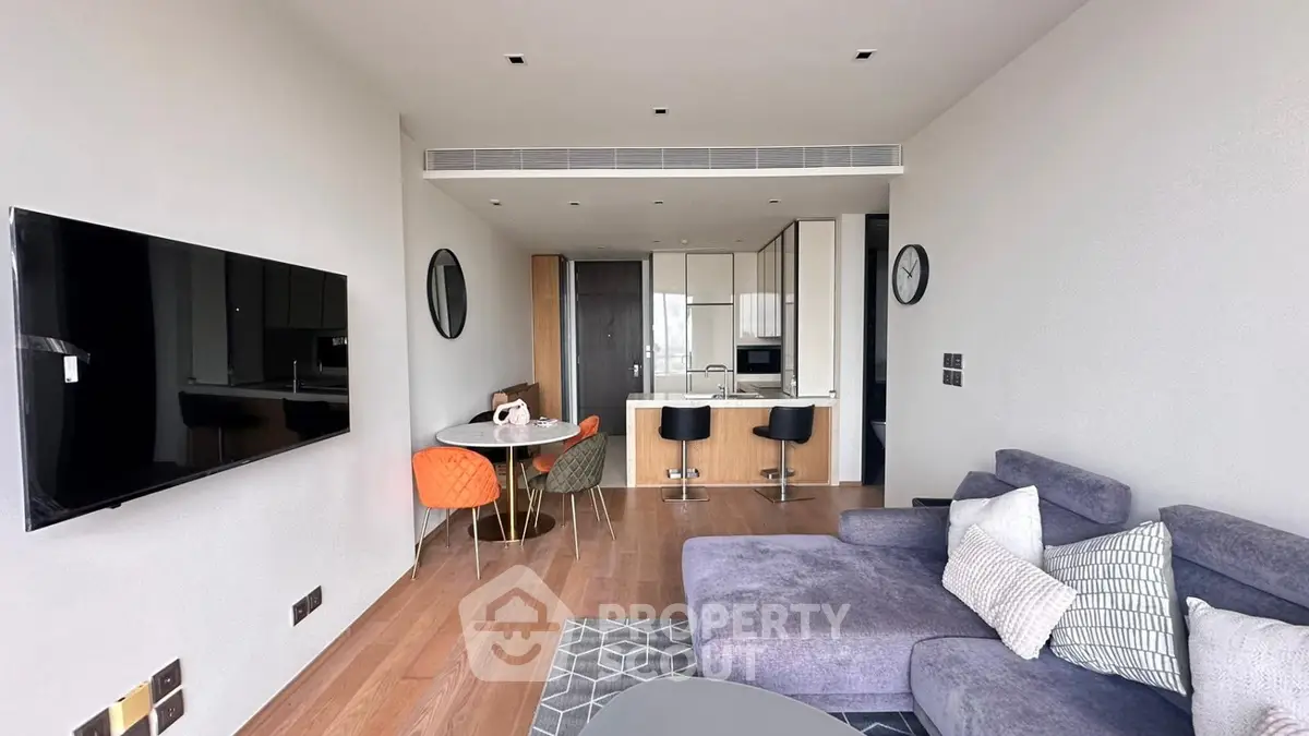 Modern living room with open kitchen, stylish furniture, and wall-mounted TV in a contemporary apartment.