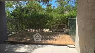 Charming outdoor patio with lush greenery and glass railing, perfect for relaxation.