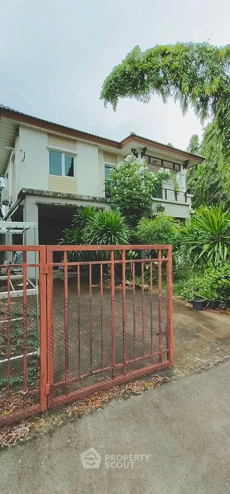 Charming two-story house with lush greenery and gated driveway, perfect for serene living.