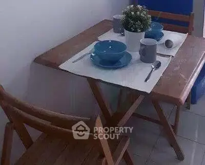 Cozy dining nook with wooden table and chairs, set for two with blue dishes and a decorative plant.