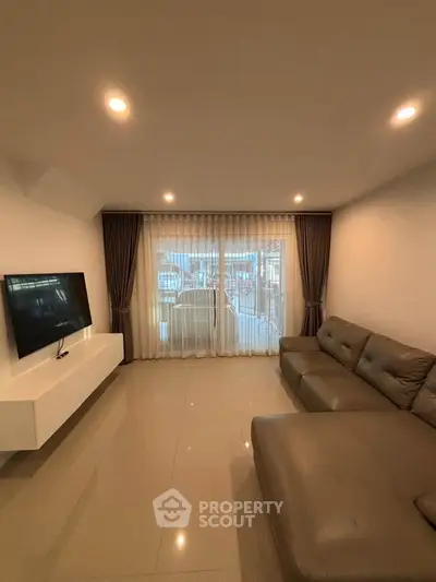 Spacious living room with modern sofa and wall-mounted TV, featuring large windows and elegant curtains.