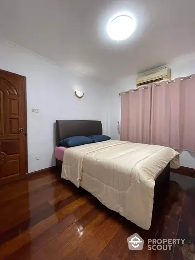 Cozy bedroom with polished wooden flooring, comfortable queen-sized bed, and built-in air conditioning unit, perfect for restful nights.