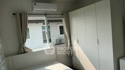 Bright bedroom with large window and white wardrobe, offering a cozy and inviting atmosphere.