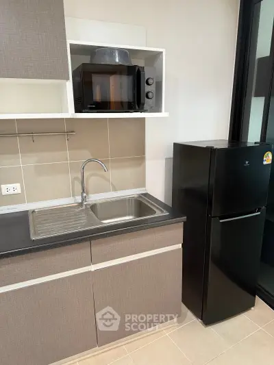 Modern kitchen with sleek cabinetry, microwave, and refrigerator in a stylish apartment.