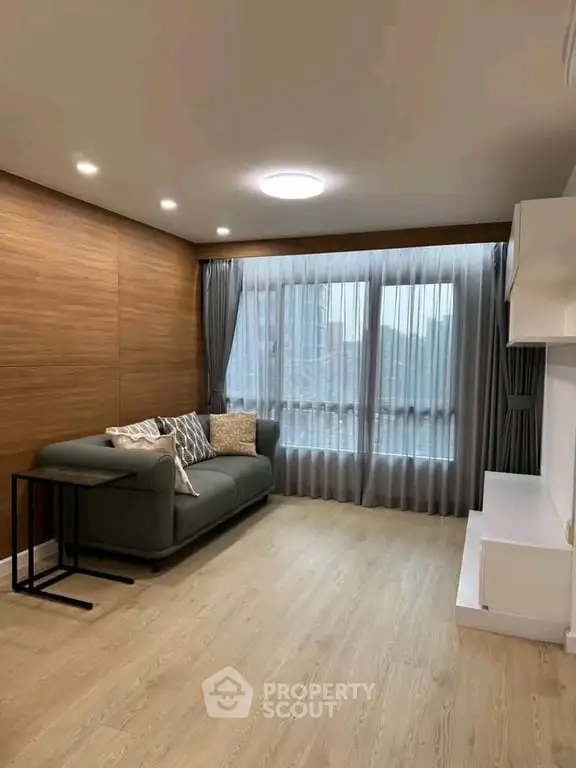 Modern living room with stylish sofa and large window, featuring elegant wooden flooring and contemporary lighting.