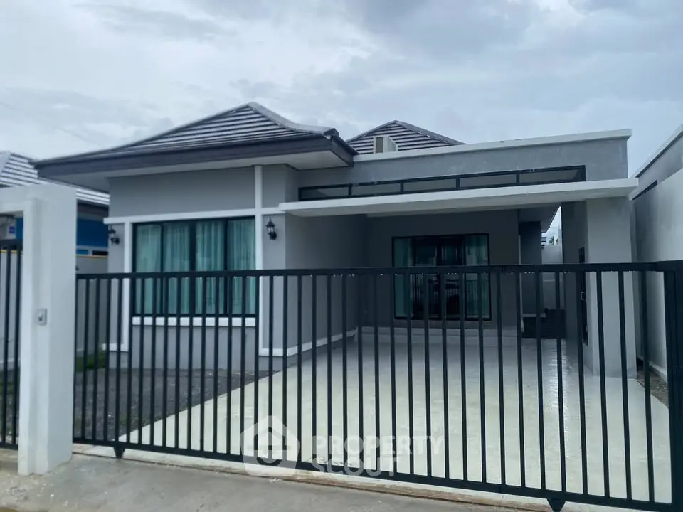 Modern single-story house with sleek design and gated driveway under cloudy sky.
