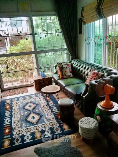 Charming living room with cozy seating and vibrant decor, featuring large windows and lush garden view.
