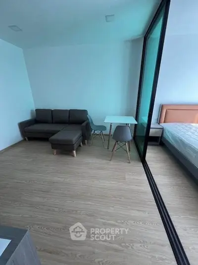 Modern apartment with sleek living room and bedroom separated by glass partition, featuring stylish furniture.