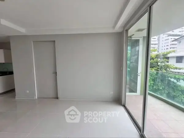 Spacious modern living room with large glass doors leading to a balcony, offering a serene view.