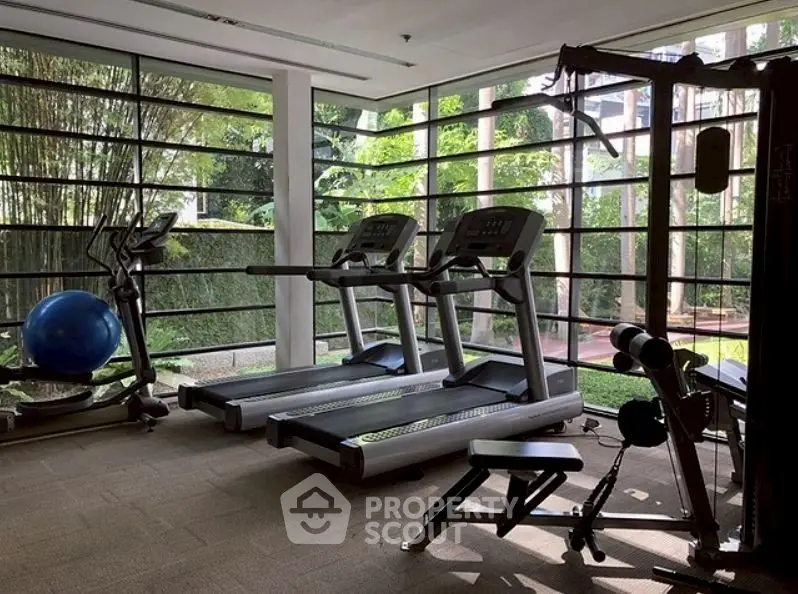 Modern gym with treadmills and exercise equipment in a bright, glass-walled room overlooking greenery.