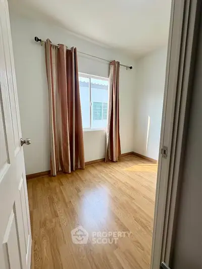 Bright bedroom with wooden flooring and large window for natural light.