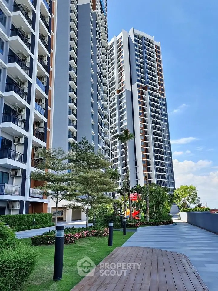 Modern high-rise residential buildings with lush landscaped gardens and clear blue sky.