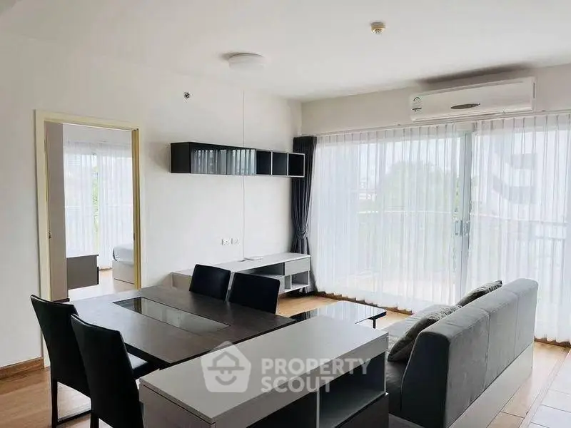 Modern living room with sleek furniture and large windows offering natural light and balcony access.