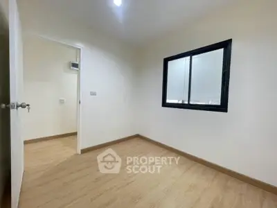 Spacious empty room with wooden flooring and large window, perfect for customization.