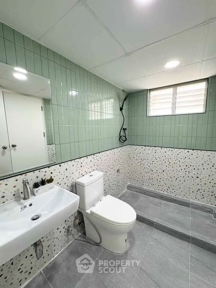 Modern bathroom with green tiles and terrazzo wall, featuring a sleek white sink and toilet.