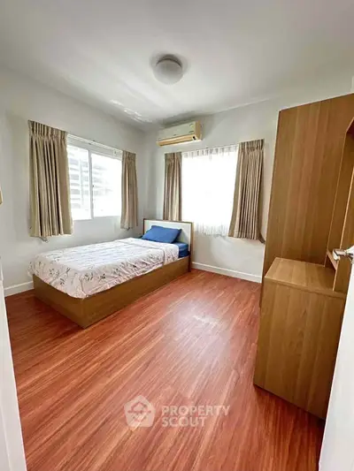 Cozy bedroom with wooden flooring and ample natural light from large windows.