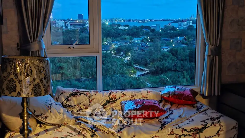 Cozy bedroom with stunning city view through large window, featuring elegant decor and plush bedding.