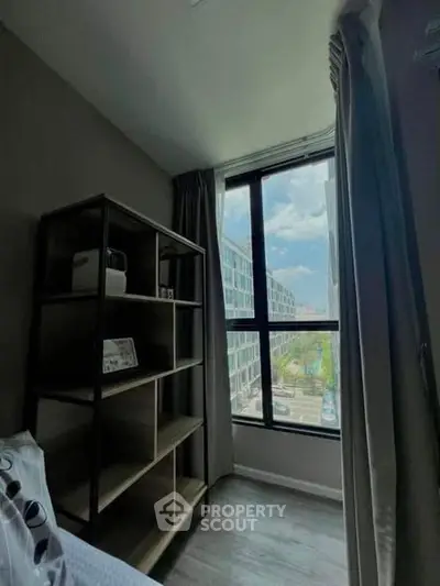 Cozy bedroom with large window offering a stunning city view, featuring modern shelving and elegant curtains.