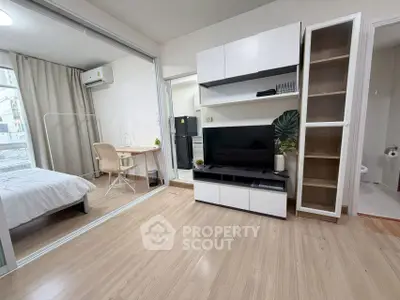 Modern apartment interior with open living room and bedroom, featuring sleek furniture and natural light.