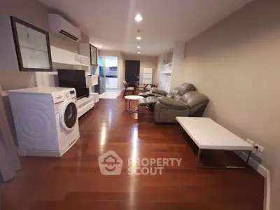 Spacious living room with modern furniture and hardwood floors, featuring a washing machine and sleek decor.