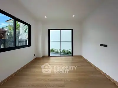 Spacious empty room with wooden flooring and large windows, perfect for customization.