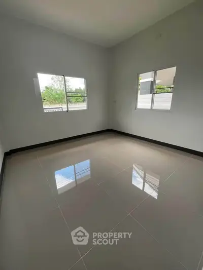 Spacious empty room with glossy tiled floor and large windows offering natural light.