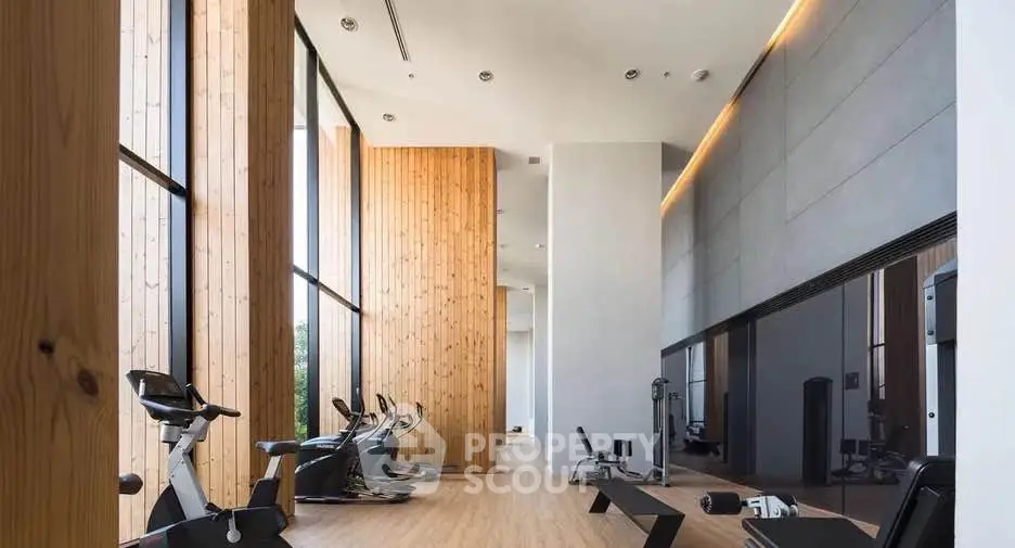 Spacious modern gym with wooden accents and large windows in luxury building.