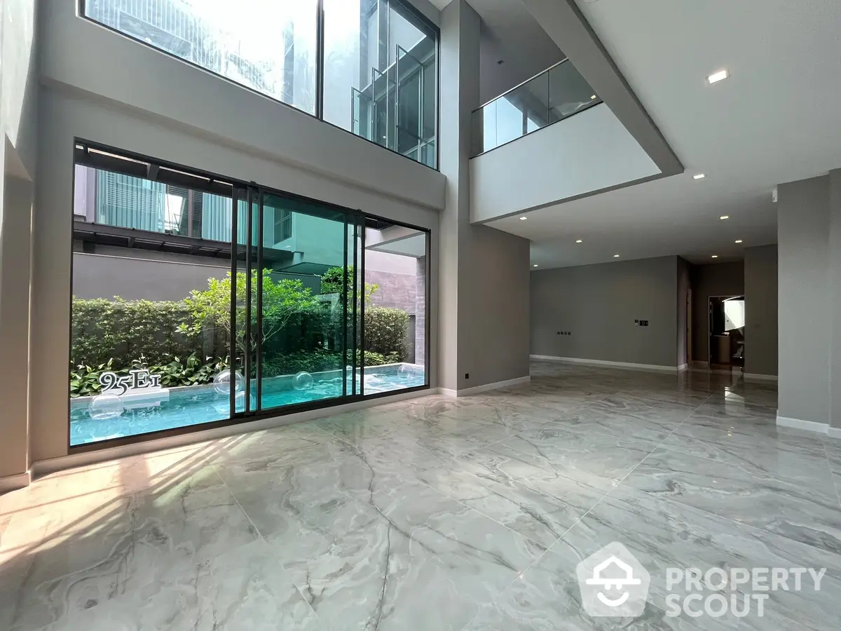 Expansive modern living room with high ceilings, large windows offering a view of the pool, and luxurious marble flooring.