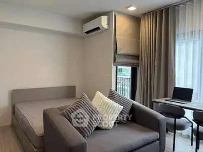 Modern studio apartment with cozy sofa, bed, and workspace near window.