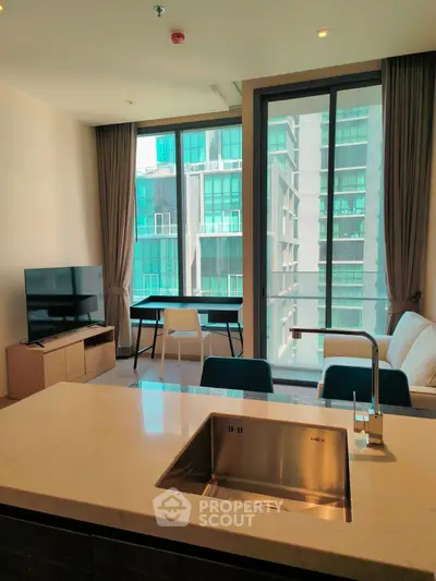 Modern living room with large windows and city view, featuring sleek furniture and open kitchen layout.
