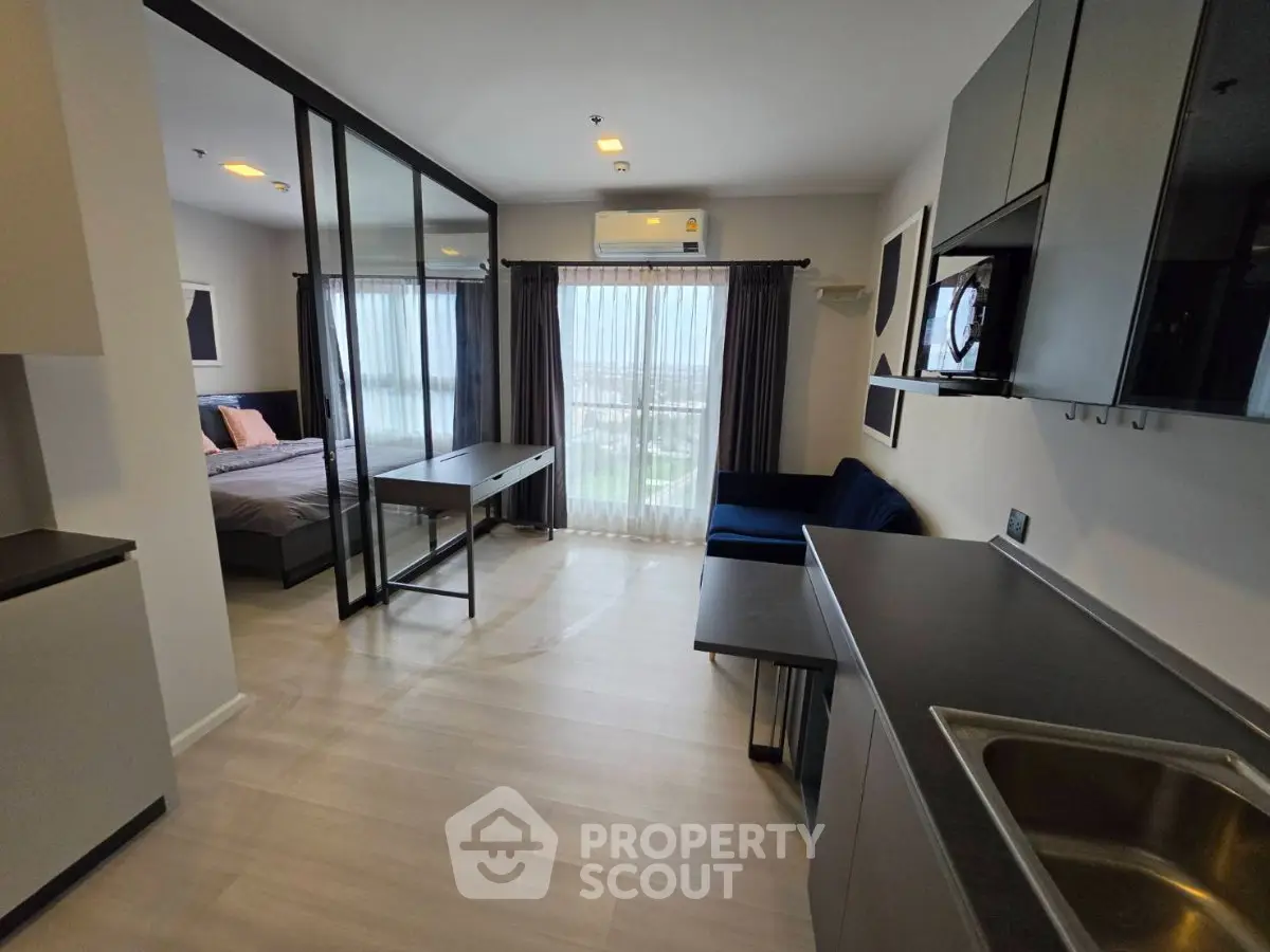 Modern studio apartment with open layout, featuring a sleek kitchen and cozy living area with large windows.
